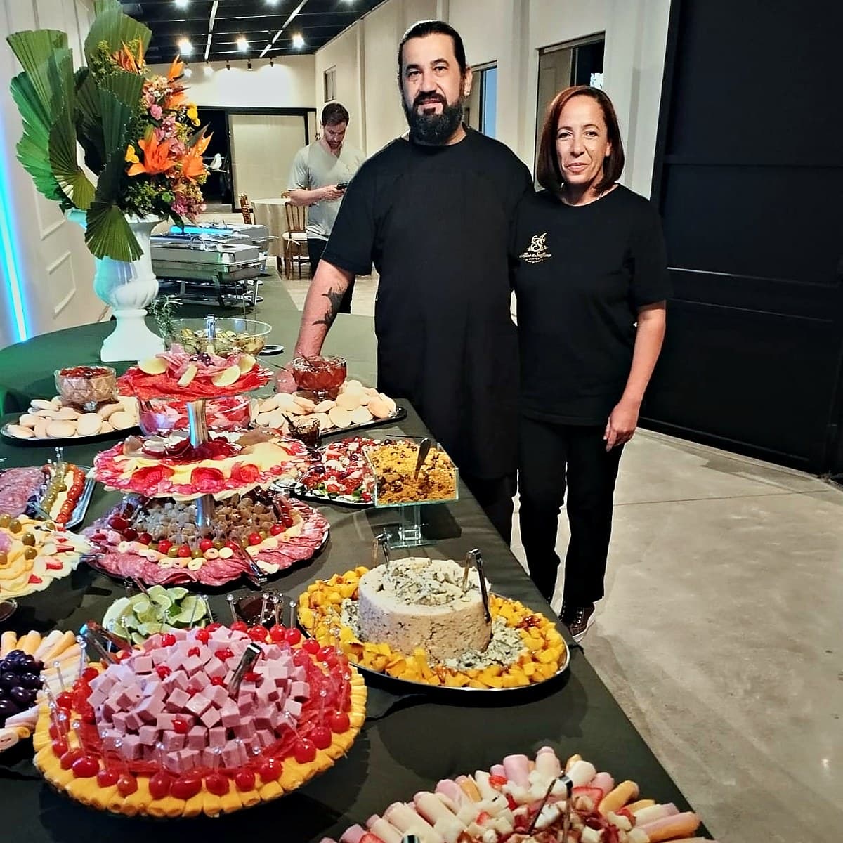 Proprietários do AS Buffet ao lado de uma mesa de frios e saladas montada para um evento