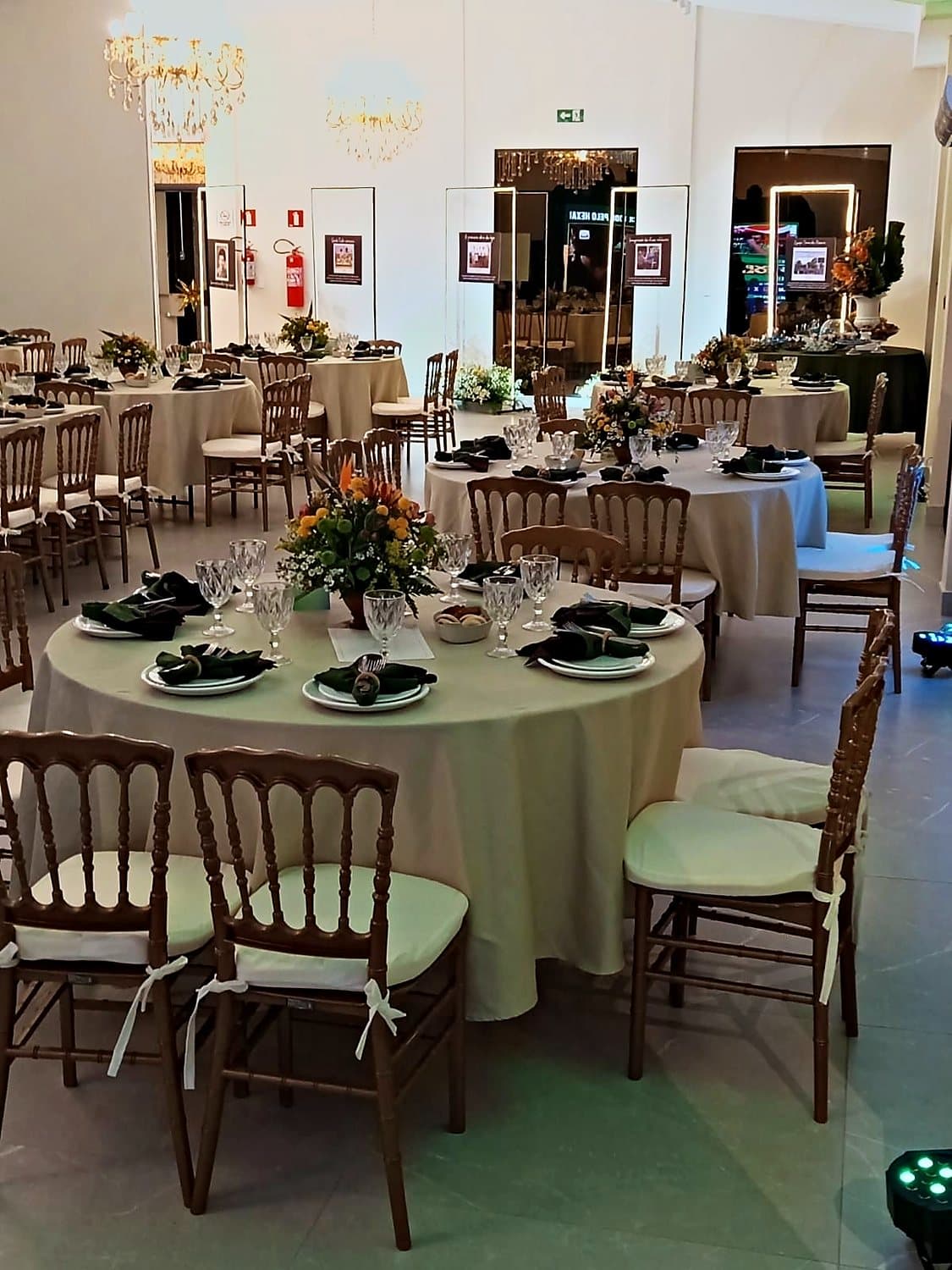 Salão de casamento com mesas redondas postas e lustre de cristal