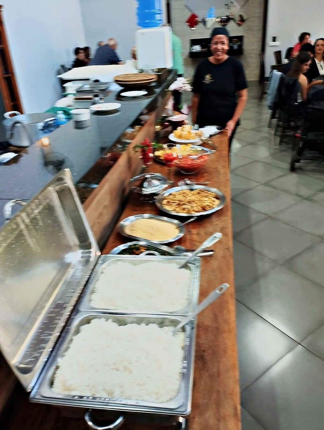Buffet completo montado no salão, com convidados ao fundo