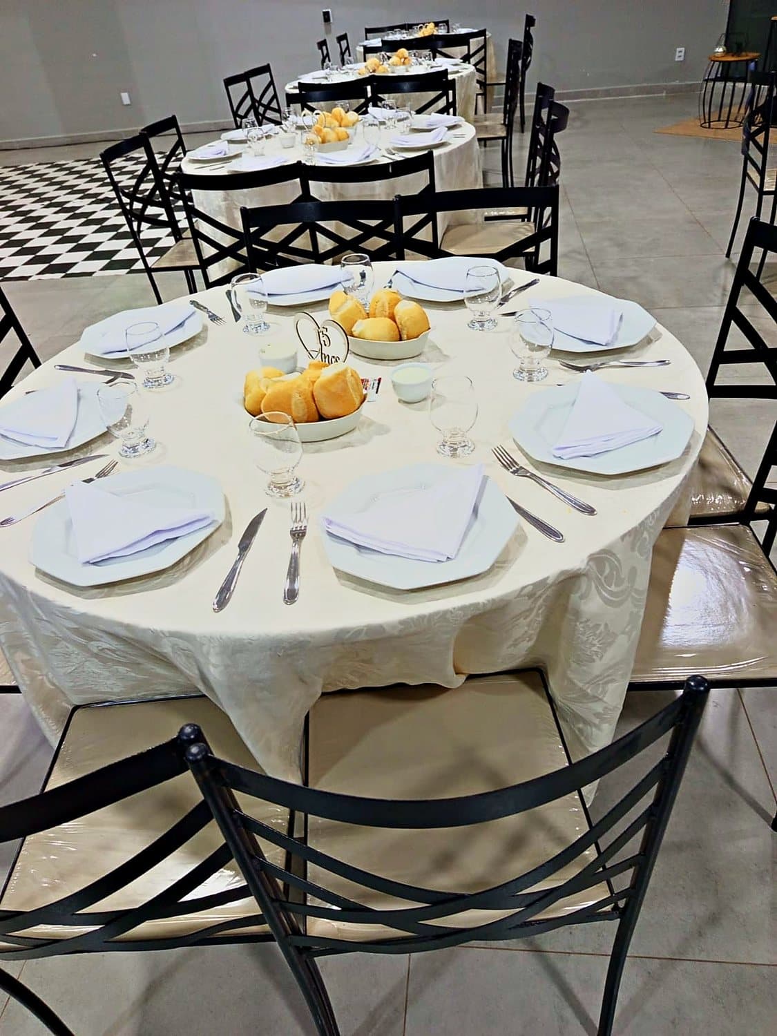 Mesa redonda posta com toalha clara e pães de entrada
